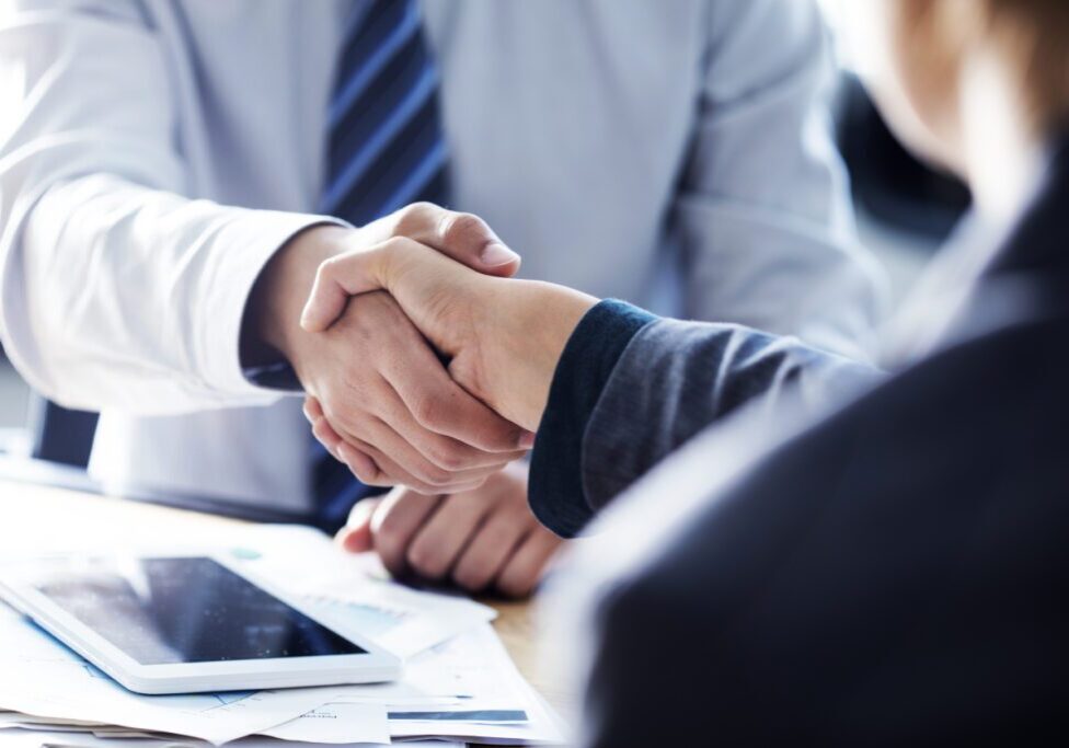 Business handshake over a desk with tablet.